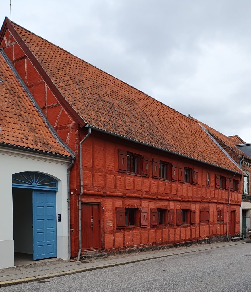 Ein rotes Fachwerkaus, daneben ein weißes Haus mit einem blauen Tor